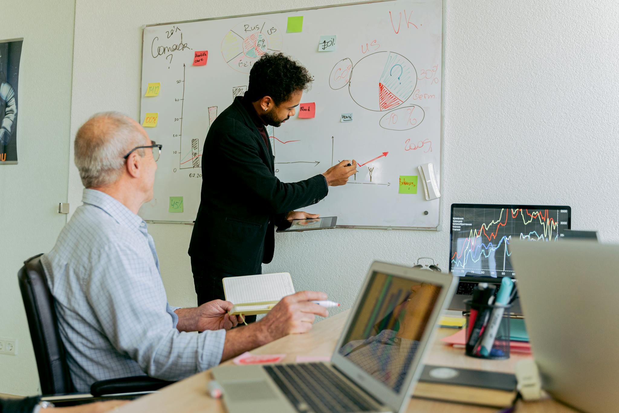 Two professionals discuss business strategy using charts and laptops.